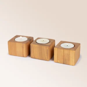 L'image montre trois Minis Kandelas, de petits bougeoirs en bois disposés côte à côte. Chacun de ces bougeoirs cubiques est fabriqué en bois avec une finition naturelle et est conçu pour accueillir une bougie chauffe-plat. Les formes épurées et les lignes simples des bougeoirs mettent en valeur leur design authentique et moderne, ajoutant une touche de charme et de chaleur à tout intérieur. Parfaits pour créer une ambiance cosy dans diverses pièces de la maison, ces petits bougeoirs bois sont à la fois élégants et éco-responsables.