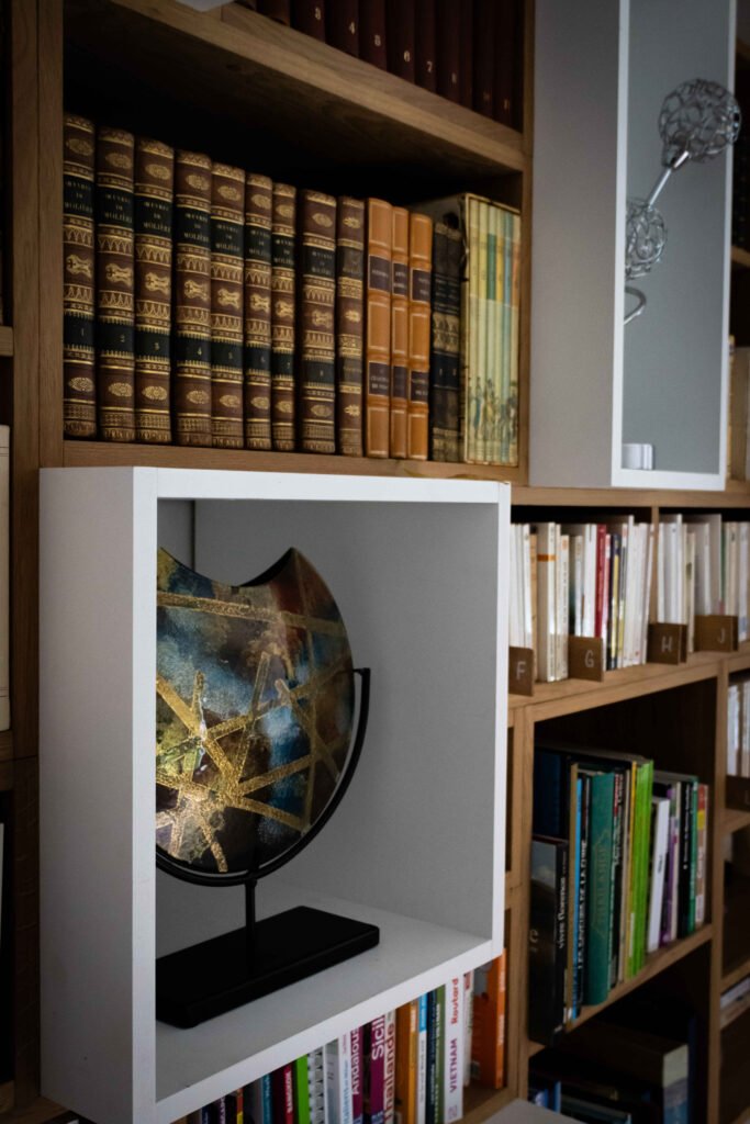 Globe décoratif doré dans un module blanc, surmonté de livres reliés anciens et accompagné d'une sculpture florale
