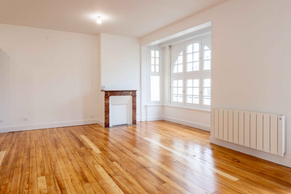 Pièce lumineuse avec cheminée en marbre rouge, fenêtre en arc et parquet ancien restauré, style haussmannien