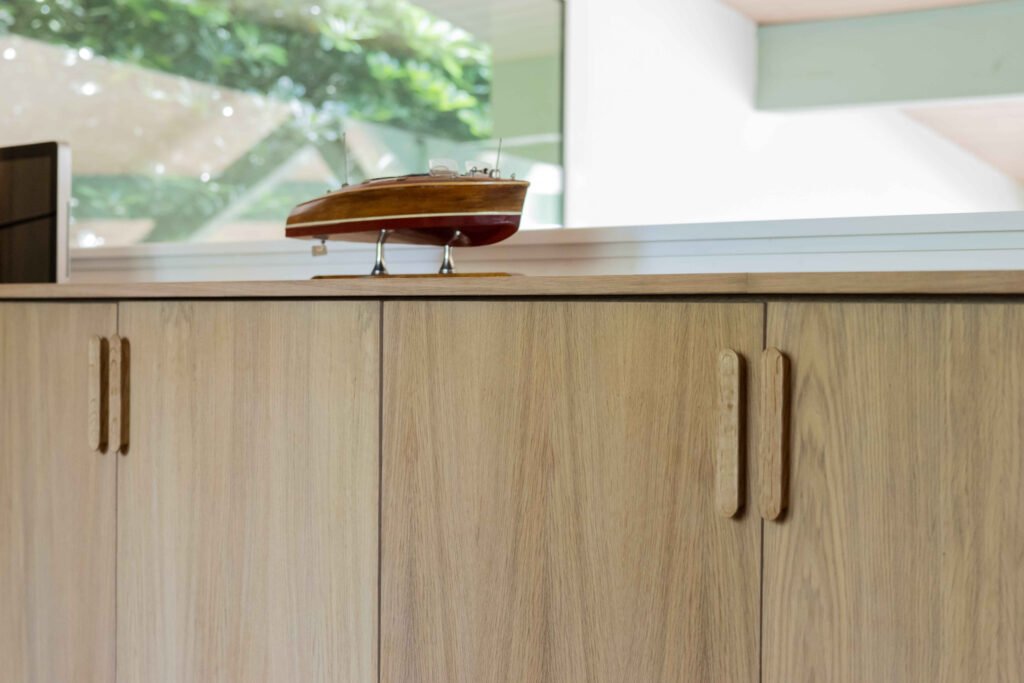 Meuble de rangement en chêne clair orné d'une maquette de bateau en bois, poignées sculptées intégrées