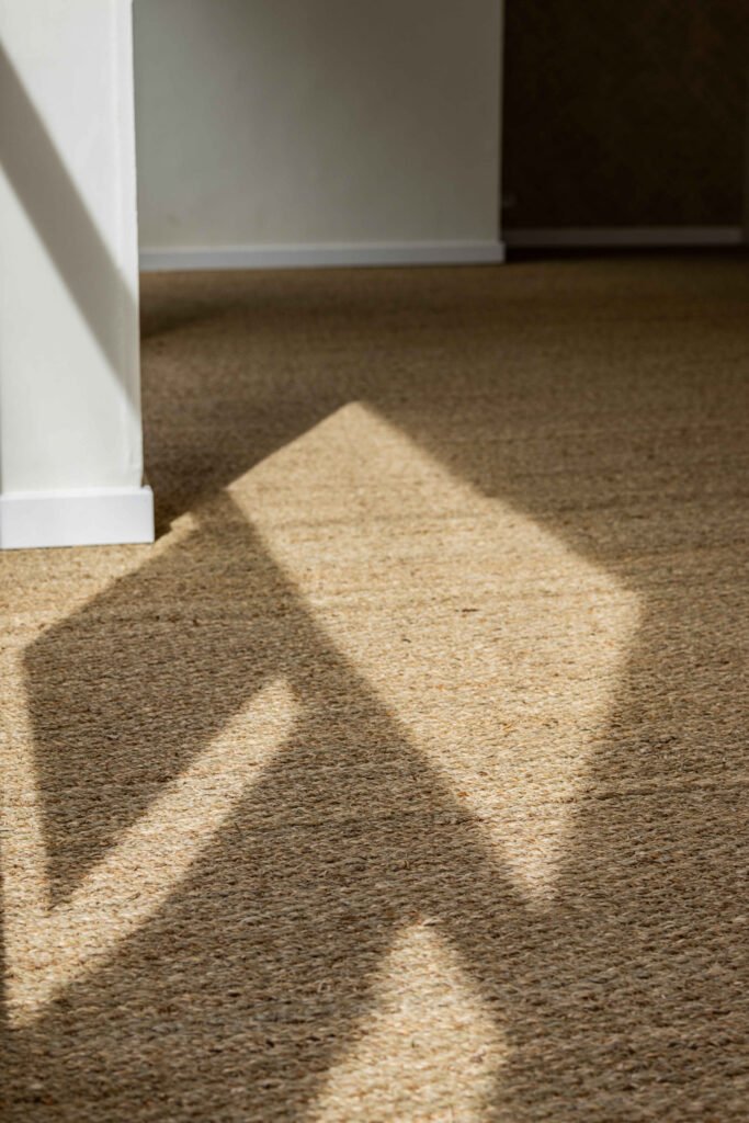 Motif géométrique d'ombre projetée sur un tapis beige, créant des lignes diagonales distinctes près d'une plinthe blanche