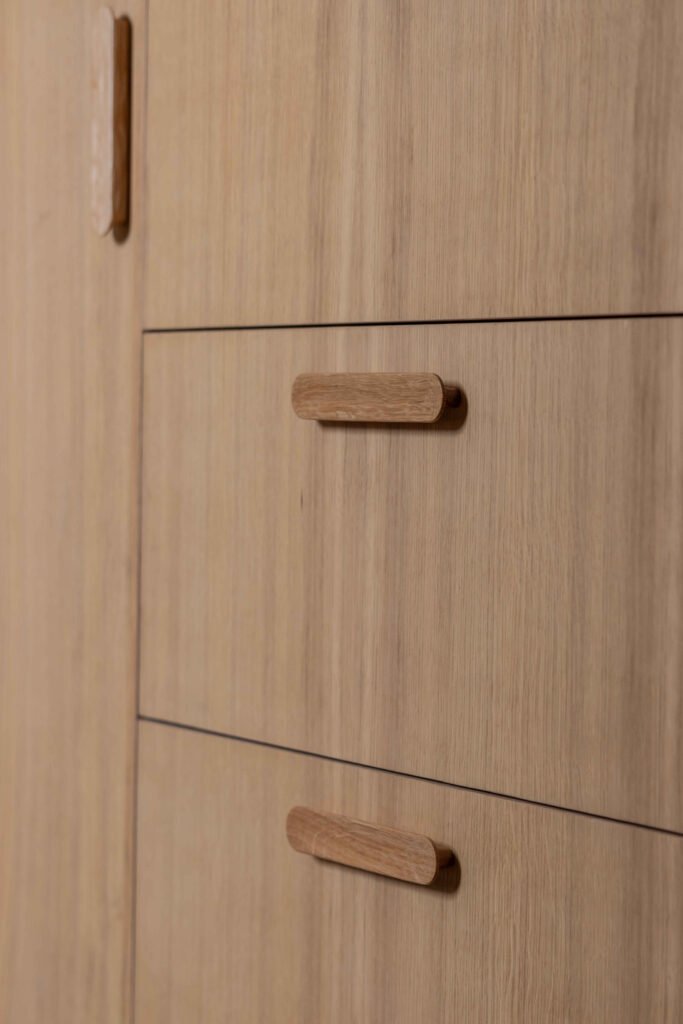 Gros plan sur des poignées en chêne massif sculptées directement dans les portes de placard